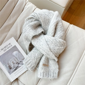 Detail of light gray thick knit scarf featuring a small gold Doria Dore metal plaque