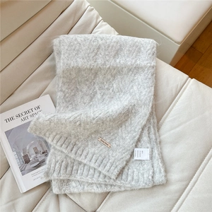 Detail of light grey knit scarf showing alpaca blend texture and metallic brand tag