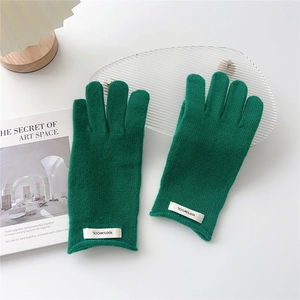 Detailed view of dark green wool knit gloves with white 100% wool material label