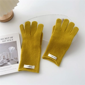 Detail of mustard yellow knit gloves showing 100% wool label and ribbed texture