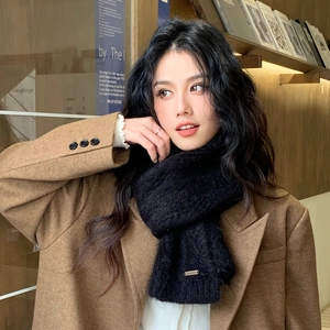 Detail of thick black knit scarf with small metal logo worn with brown wool coat