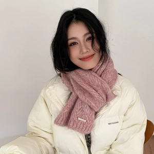 Close-up of pink cable knit scarf with a metallic brand tag on soft winter fabric