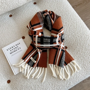 Detail of knit scarf with orange and black plaid pattern, tassels, and brand label