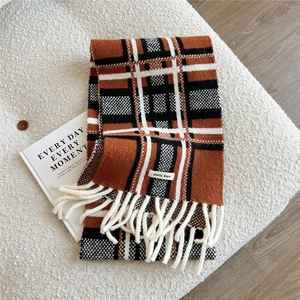 Detail of soft knit plaid scarf in burnt orange and black with white fringe and brand label
