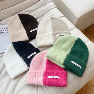 Two-tone knitted beanie hats with ribbed cuffs and contrast colors on a textured sofa