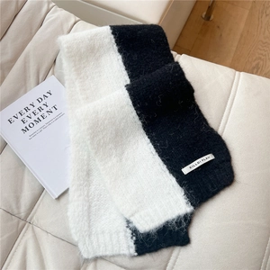 Close-up of thick black and white knit scarf with brand label on a soft leather sofa