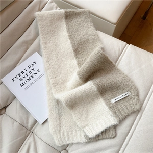 Detail of knit scarf with bicolor beige and khaki blocks on a white quilted leather surface