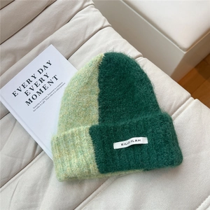 Close-up of thick green two-tone knit beanie with branded woven label on soft texture
