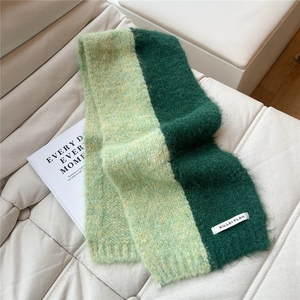 Detail view of two-tone green knit scarf with fluffy texture on a white leather sofa