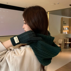 Close-up of dark green cable knit scarf and gloves set with a small branded woven label