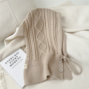 Detail of beige cable-knit balaclava with buttons, drawstring, and soft wool texture