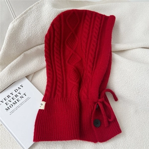 Detail of red cable knit balaclava with decorative buttons and brand tag on white fabric