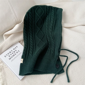 Detail of dark green cable knit balaclava with button closure and drawstring on blanket