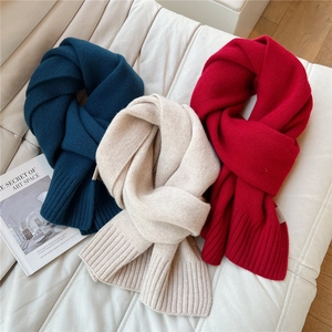 Dettaglio di sciarpe in lana a maglia spessa in blu, crema e rosso su divano bianco