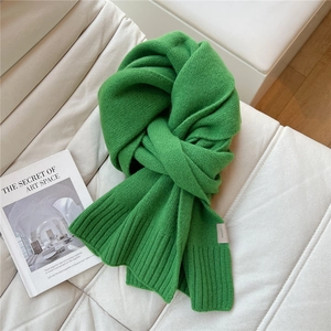 Dettaglio di sciarpa in lana verde brillante con trama a maglia su divano bianco