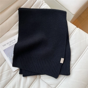 Dettaglio di sciarpa in 100% lana con trama a maglia spessa ed etichetta materiale