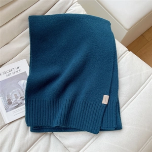Dettaglio di una sciarpa di lana blu petrolio a maglia su un divano bianco elegante