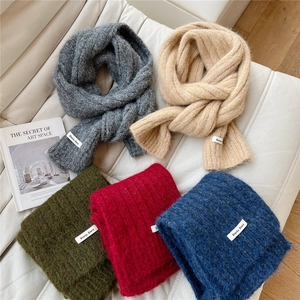 Thick solid color knitted winter scarves in multiple colors on a white leather sofa