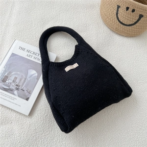 Detail of minimalist black knit handbag showing thick texture and woven rectangular label