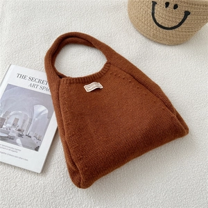 Detail of a brown knit hobo bag with a white woven label on warm textured fabric