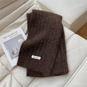 Close-up of soft dark brown knit scarf texture with white woven label on leather surface