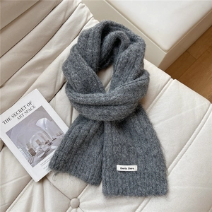 Detail of soft charcoal grey knitted scarf with brand label on a cozy white sofa