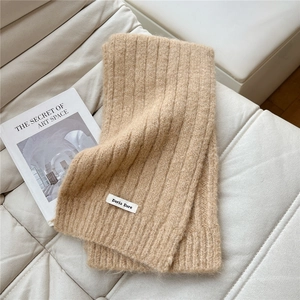 Close-up of beige chunky knit scarf showing ribbed texture and stitched label on sofa