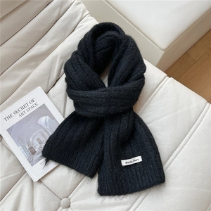 Close-up of black knitted scarf with rib texture and elegant brand label on white leather