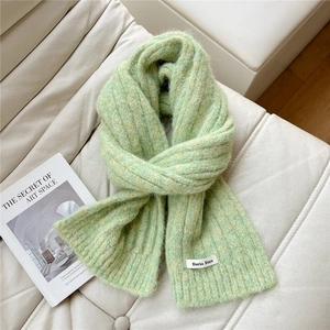 Detail of light green chunky knit scarf with woven label on a soft quilted sofa