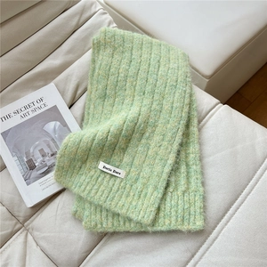 Close-up of thick rib-knit scarf in light green with woven brand tag on soft sofa