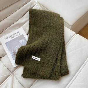 Close-up of deep forest green knit scarf with soft fluffy texture and white woven label