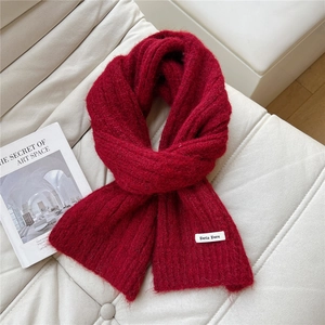 Close-up of deep red knitted scarf texture and white brand label on soft white sofa