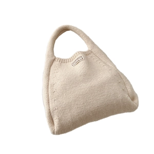 Minimalist beige knitted hobo tote bag with a woven texture and rectangular fabric label