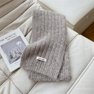 Close-up of thick oatmeal knit scarf texture and brand label on a soft leather sofa