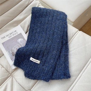 Detail shot of navy blue chunky knit scarf with white label on ivory leather sofa
