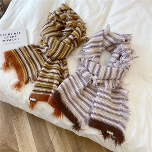 Winter striped knit scarf with long tassels in yellow and purple on a soft white bed