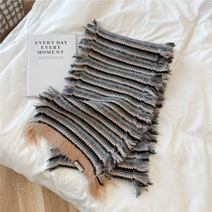 Detail of grey striped knit scarf with long fringe on a cozy white fabric background