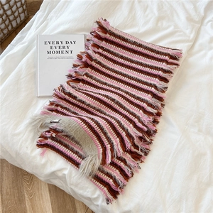 Detail of colorful striped knit scarf with long decorative fringe on white bedding
