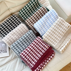 Various colors of houndstooth knit winter scarves displayed on a soft white sofa