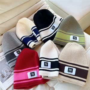Close-up of assorted striped knit beanies with branded logo patches on a soft sofa
