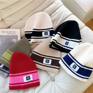 Close-up of colorful striped knit beanies with DG labels on a soft quilted surface
