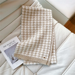 Macro detail of houndstooth knit scarf texture with a small gold metal logo accent