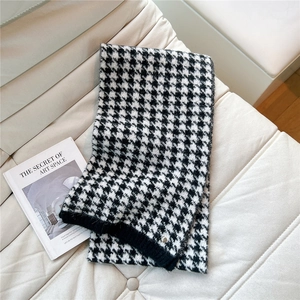 Detail of houndstooth knit scarf with ribbed edge and metal accent on a leather sofa