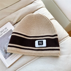 Detail shot of beige knit beanie with brown stripes and branded label on a sofa