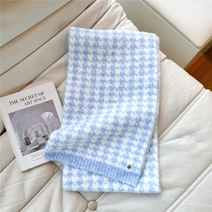 Close-up of light blue houndstooth knit scarf with soft texture and metal logo detail