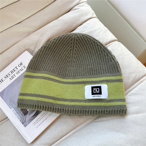 Close-up of olive knit beanie with neon stripes and branded label on a soft fabric