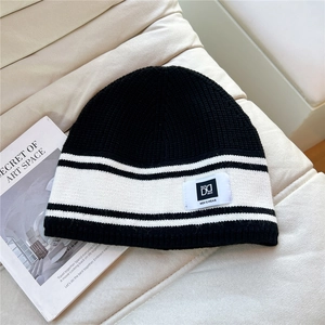 Detail of black and white striped knit beanie on white leather with logo patch