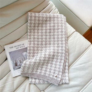 Detail of soft houndstooth scarf showing knit texture and golden emblem on beige sofa