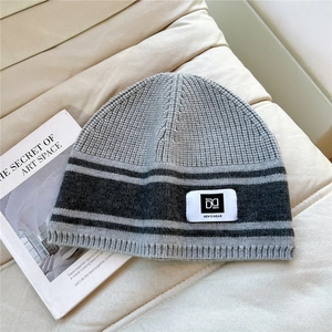 Detail of grey striped knit beanie with brand label on a textured sofa background
