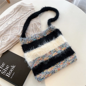 Détail du sac cabas en maille rayée duveteuse avec anses noires sur une table blanche